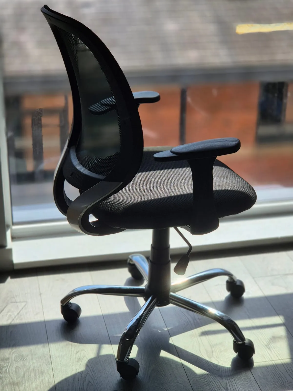A black mesh office chair on castors, rescued from the bin store, standing in the light by a window.